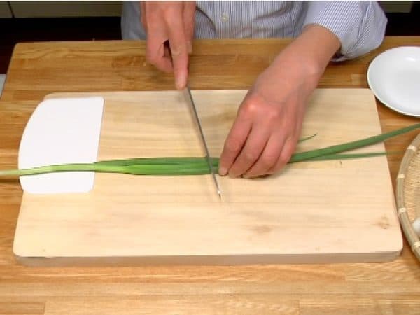 Let's prepare the toppings for the udon noodles. Chop the spring onion leaves into fine pieces.