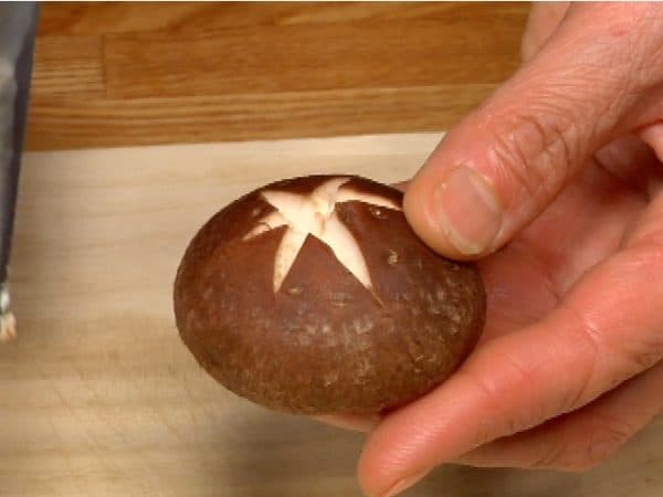 Chop off the stem of the shiitake mushroom. Make a cross-shaped cut on the cap of the mushroom.