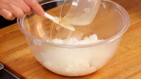 Tiếp theo, chuẩn bị cơm nóng mới nấu. Đảo giấm dùng cho cơm cuộn (sushi) kĩ và đổ nó lên cơm nóng. Nếu cơm nguội, nó sẽ không ngấm tốt giấm dùng cho cơm cuộn (sushi).