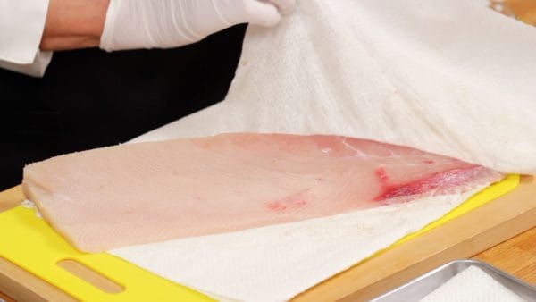 Mari menyiapkan ikan yellowtail kualitas sashimi yang juga dikenal dengan buri. Serap air pada ikan dengan tisu dapur.