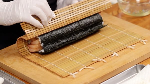 Tarik sushi gulung ke arah Anda, lepaskan sebagian ujung tirai sushi untuk memeriksa apakah sushi tergulung dengan benar, lalu eratkan lagi gulungannya.