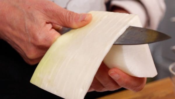 Let's prepare the side vegetables. Peel a thick layer off the daikon radish. There are a lot of pungent components and fibers near the skin so if you grate the daikon, it is better to peel the skin off for a better texture and taste.