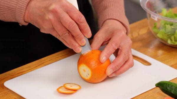 Manteniendo el Tankan en la tabla de cortar, incline la punta de la hoja del cuchillo y clávelo hacia el centro del cítrico.