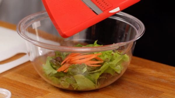 Siguiente, preparemos la ensalada. Previamente corte las hojas de lechuga verde y roja en trozos del tamaño de un bocado. Utilizando una cortadora mandolina, corte la zanahoria en tiras delgadas.
