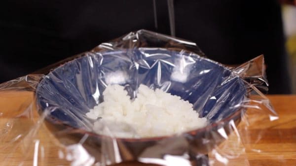 Hagamos 3 tipos de Onigiri, o bolas de arroz. Coloque una cantidad relativamente pequeña de arroz al vapor en una hoja de envoltura de plástico. Agregue un poco de sal.