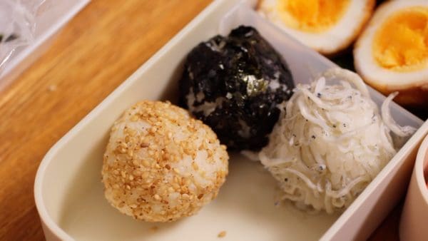 Place the onigiri rice balls with shirasu whitebait, toasted nori seaweed and sesame seeds into the bento box.