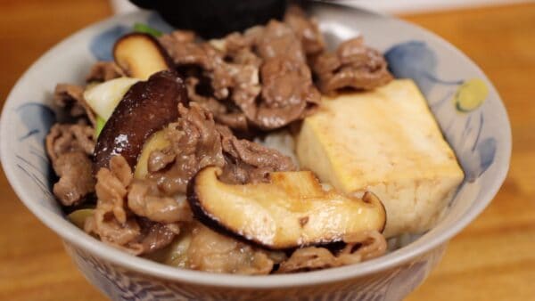 把牛肉、长葱和香菇片舀在米饭上，放在豆腐周围。