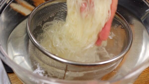 Then place the strainer into a bowl of cold water. Rub the noodles with your hands to remove any gooey film. We are showing this step on the counter just for filming so do this under running water if you are at home.