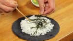 Let's make the salmon avocado bowl or poke bowl. Prepare the steamed rice on a plate and distribute the shredded nori seaweed all over.