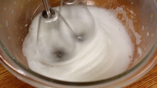 When the egg white becomes foamy and streaks begin to appear on the surface, add another 1/3 of the sugar.