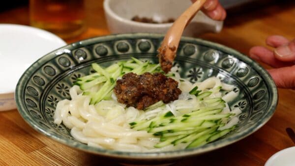 Leg netjes wat in reepjes gesneden komkommer boven op de noedels. Voeg ook de fijngesneden lenteui toe en plaats het vlees miso mengsel in het midden. 