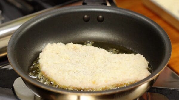 Once you hear a gentle sizzling sound, remove any excess breadcrumbs from the pork and carefully place it in the pan.