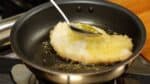 Inclinez de temps en temps la poêle et versez l'huile chaude sur le tonkatsu. Secouez la poêle pour favoriser un brunissement uniforme et répartir la chaleur uniformément.