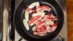 次にカレーのスープを作ります。深めのフライパンに長ねぎを入れます。豚バラ肉を重ならないように置きます。