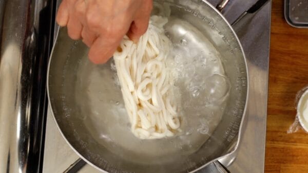 Let's boil the udon noodles. Place the frozen udon in boiling water. Release the udon just above the water to prevent it from splashing.