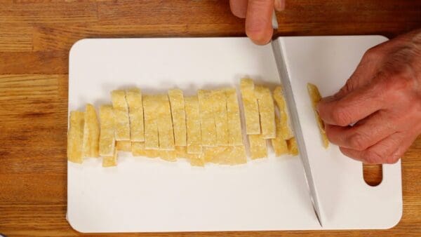 Next, cut the aburaage, thin deep-fried tofu, in half lengthwise and stack them on top of each other. Cut the aburaage into 1cm (0.4") width strips.