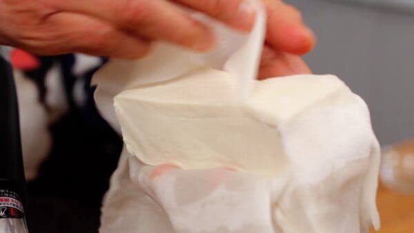 Enveloppez le tofu dans une serviette en papier épaisse et laissez-le reposer un moment au préalable pour éliminer l'excès d'eau.