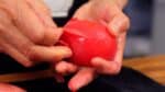 Remove the stem end and peel the skin. Soaking it in water for a few minutes makes the skin easy to peel and the tomato firm enough to cut with a knife. If it's still hard, let it soak a bit longer, as it's not safe to slice a hard, frozen tomato.